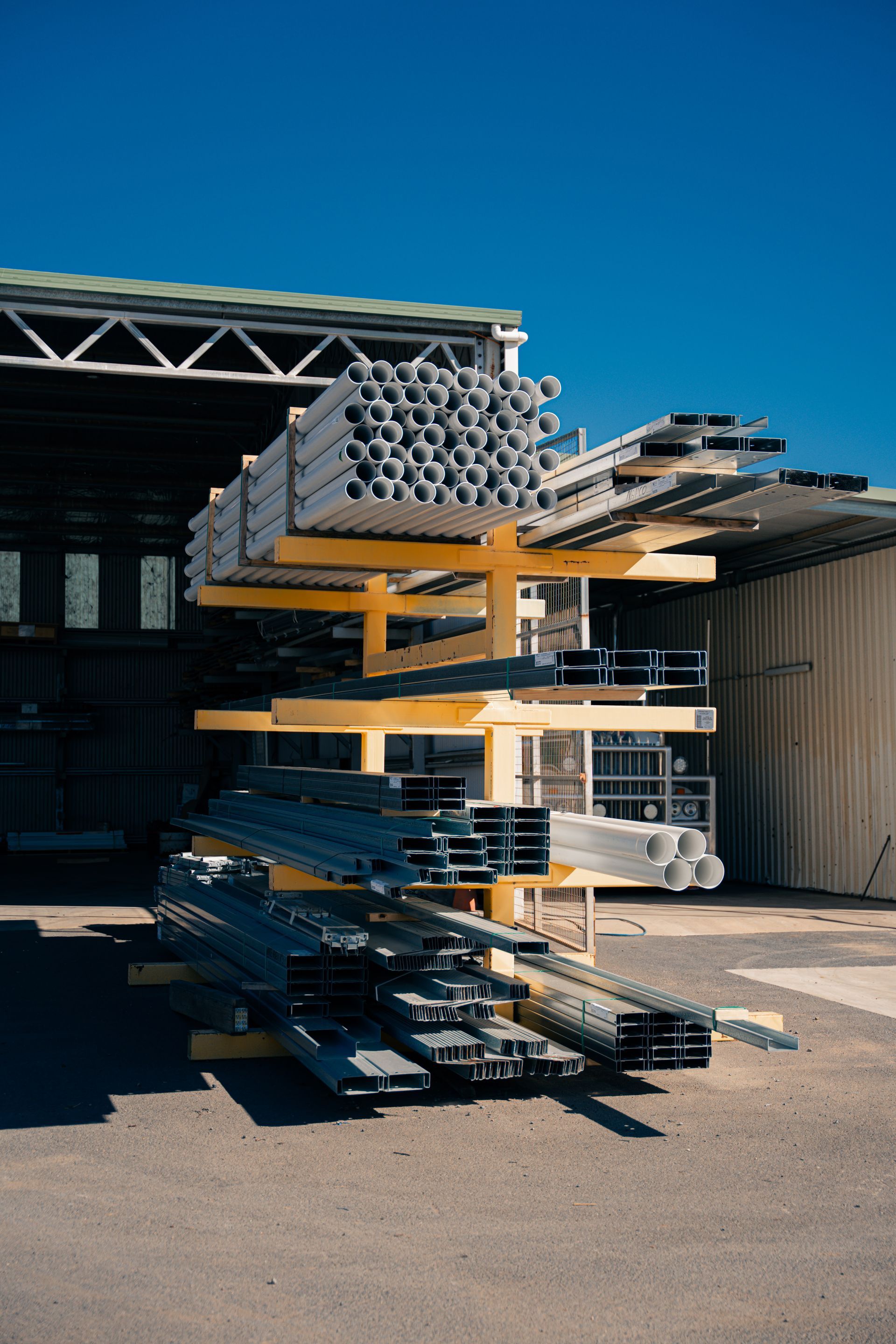 A bunch of pipes are stacked on top of each other on a rack in front of a building.