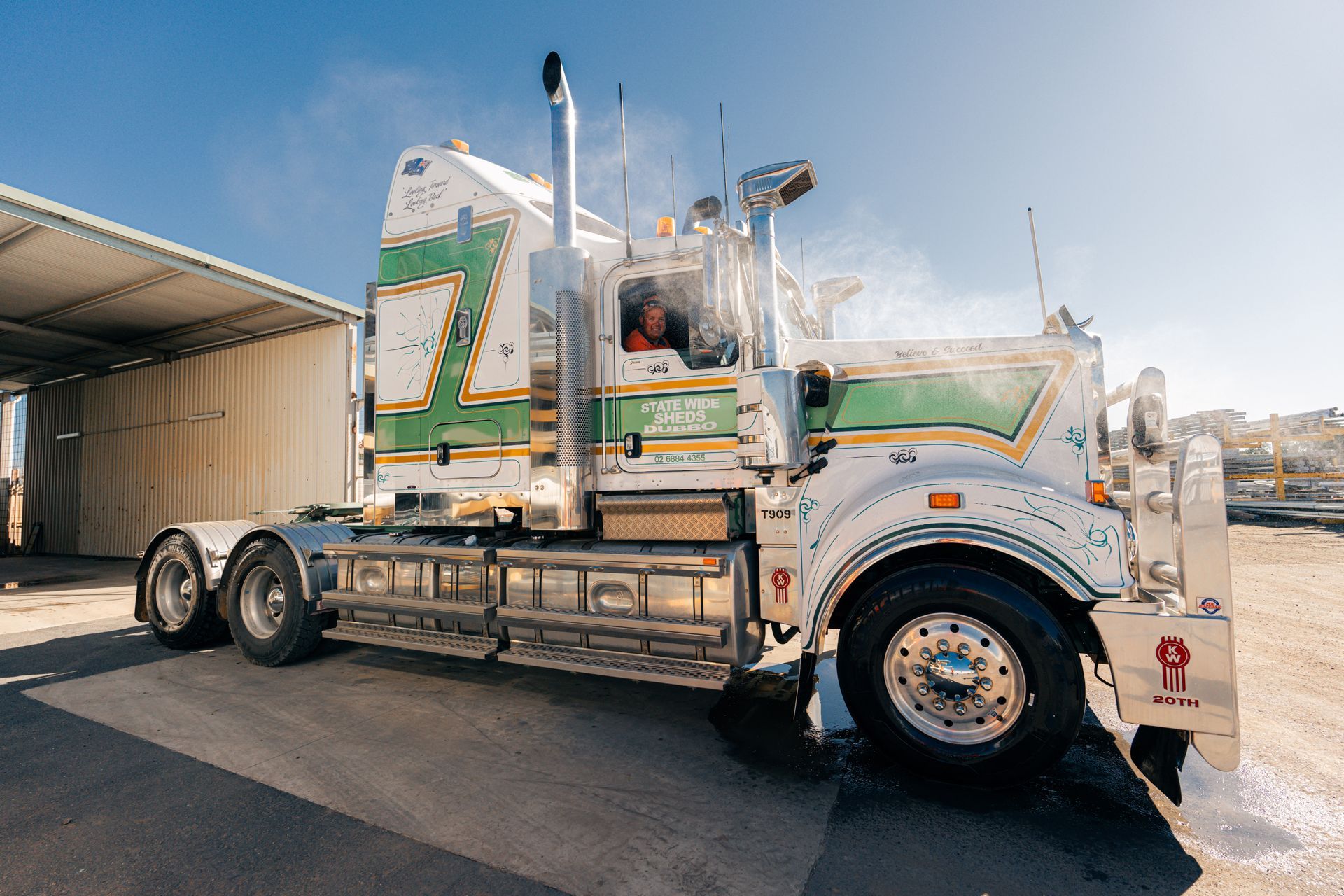 A white and green semi truck is parked in front of a building.