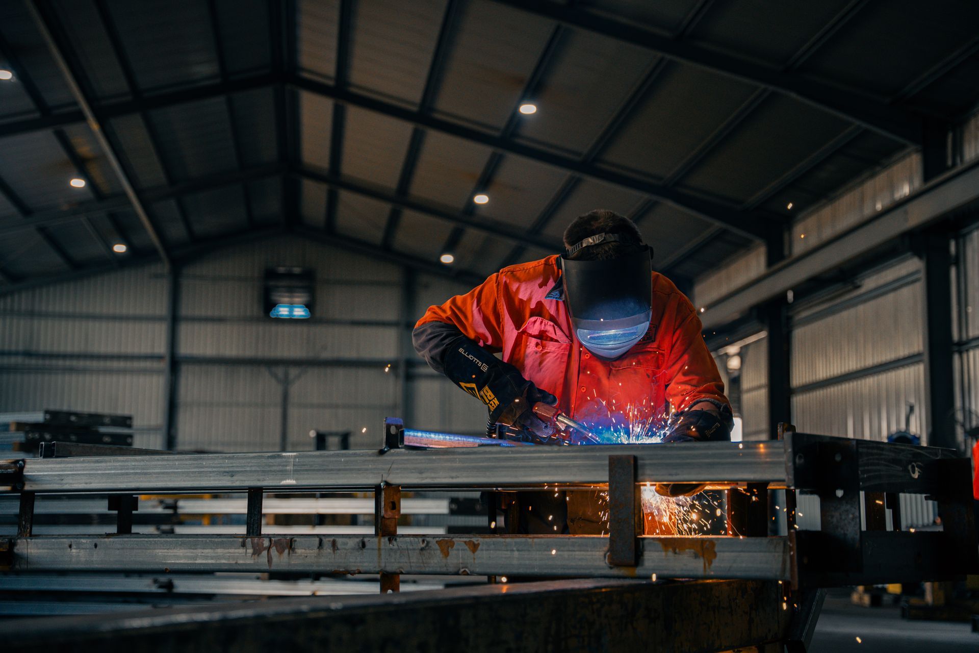 A man is welding a metal structure in a warehouse.
