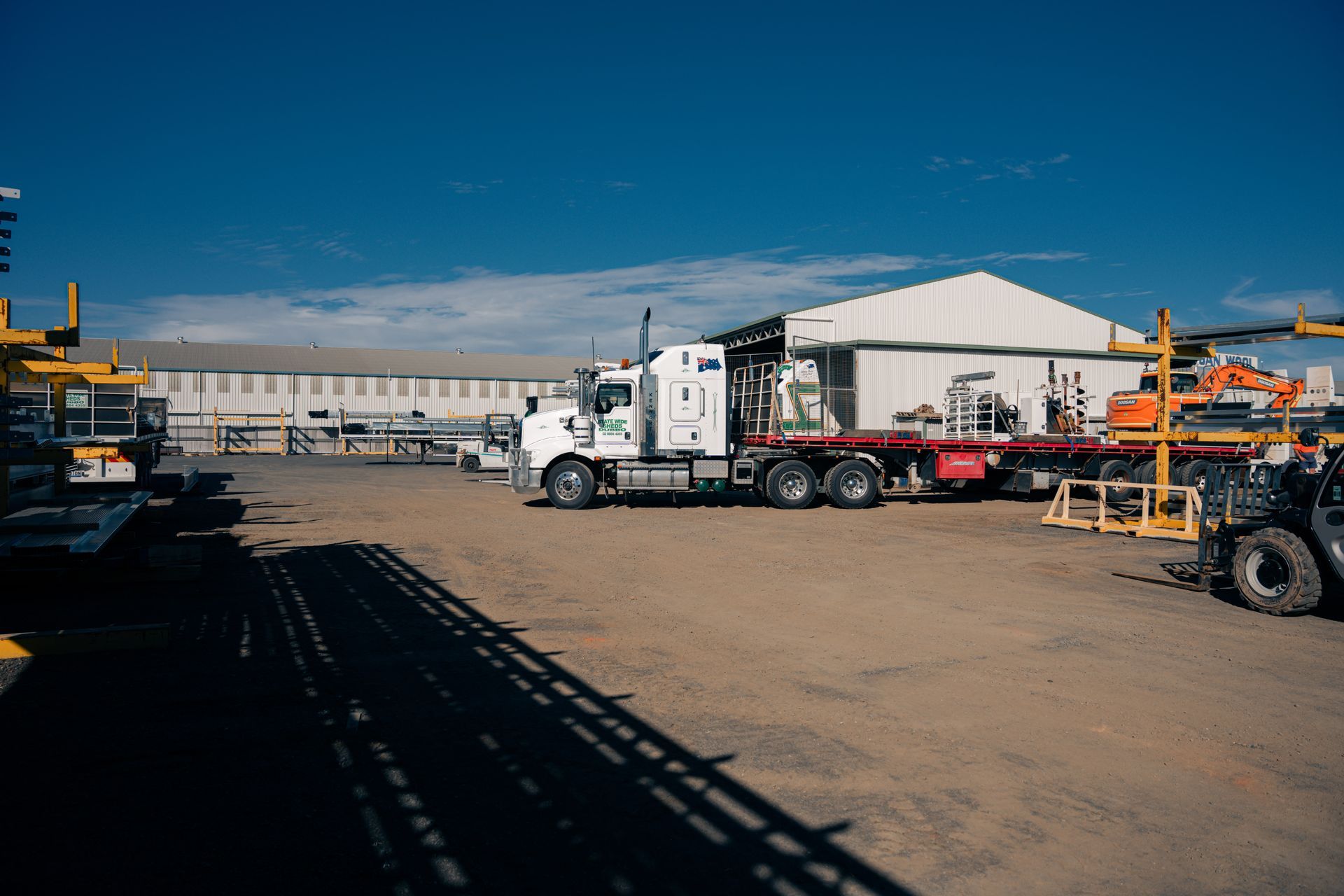 A white semi truck is parked in a dirt lot in front of a building.