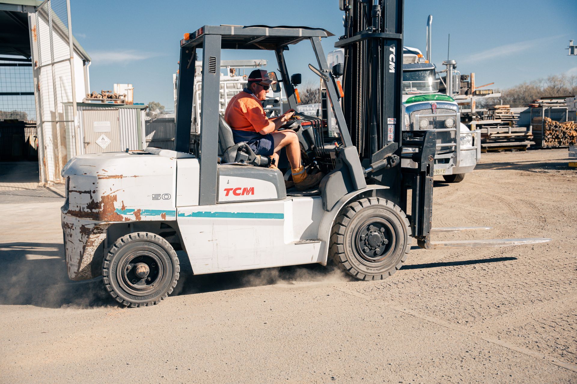 A man is driving a forklift on a dirt road.
