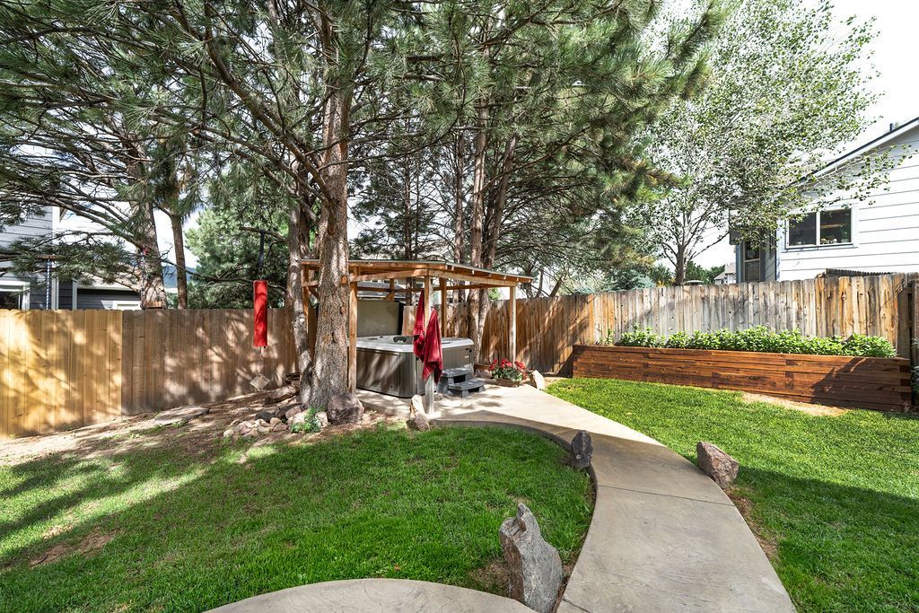 A concrete walkway leading to a backyard with a fence and trees.