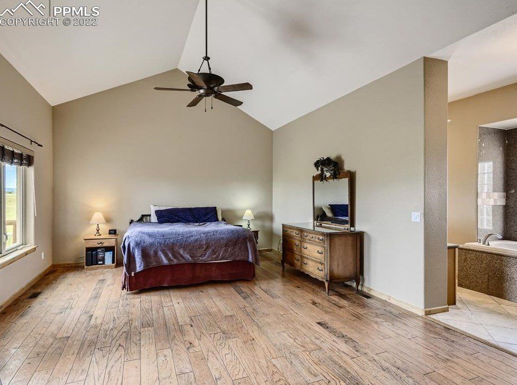 A bedroom with a large bed , dresser , mirror and ceiling fan.
