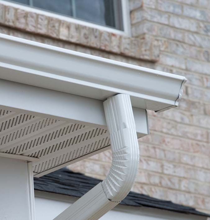 A white gutter on the side of a brick house.