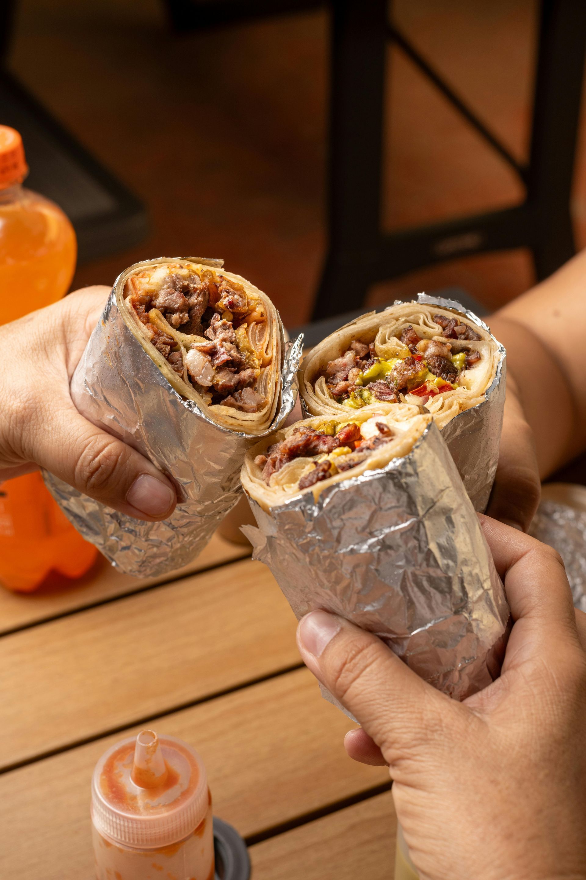 A person is holding two burritos wrapped in tin foil.
