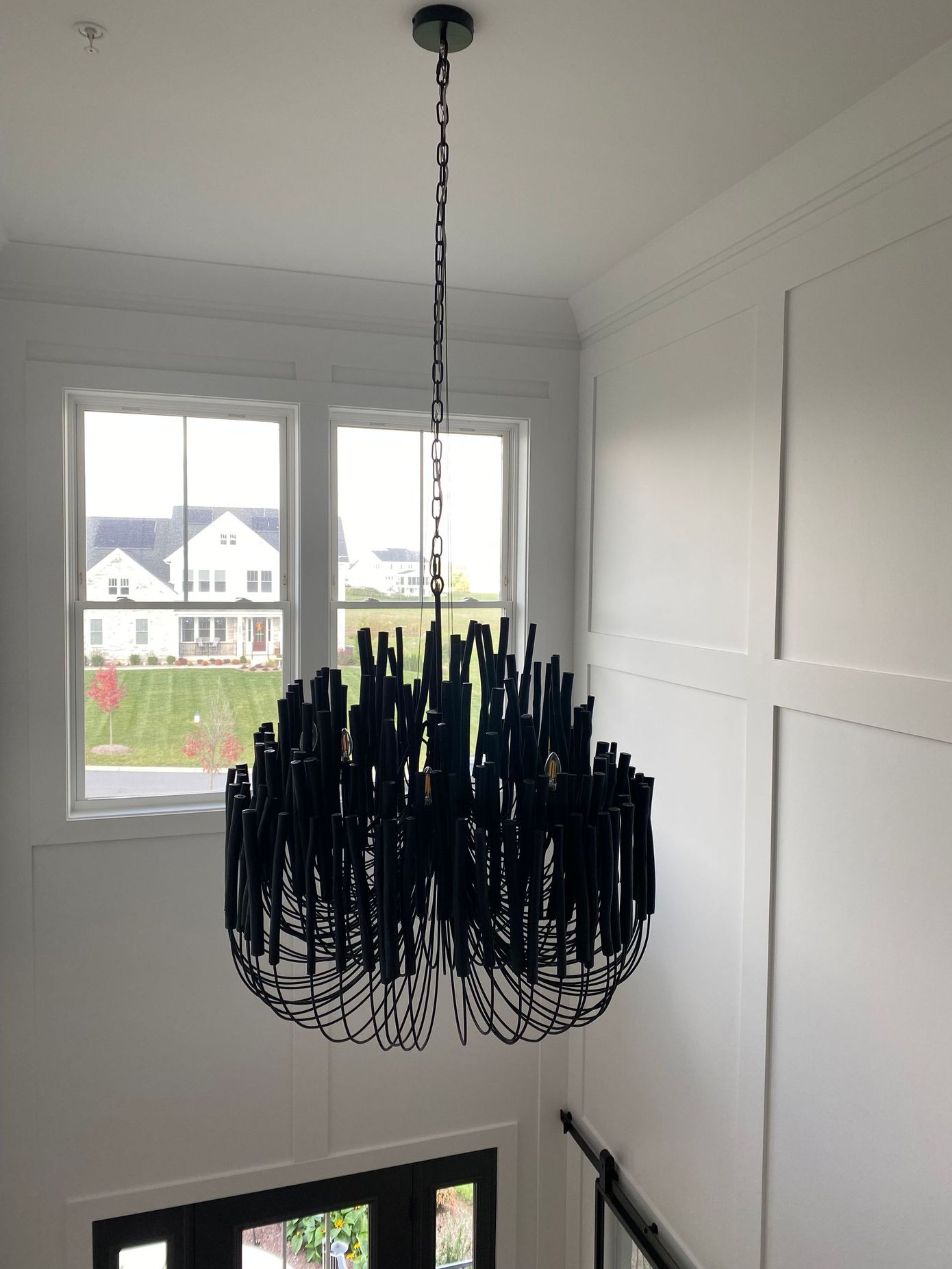 A black chandelier is hanging from the ceiling in a room with a window.