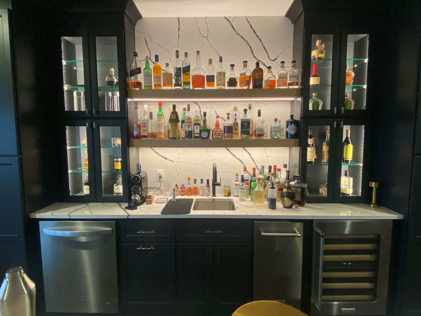 A kitchen with a bar and lots of bottles on shelves.