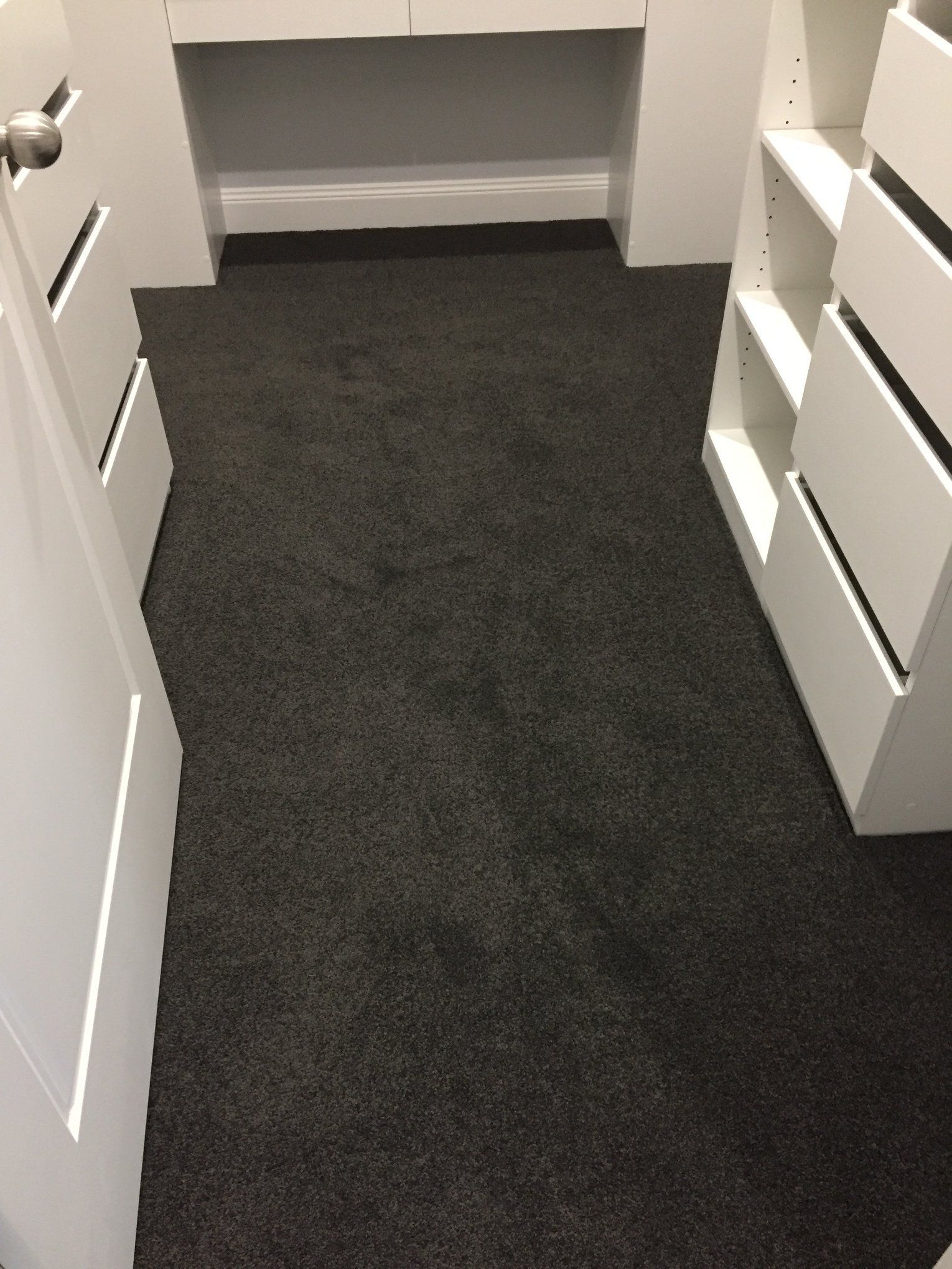 A walk in closet with a black carpet and white shelves