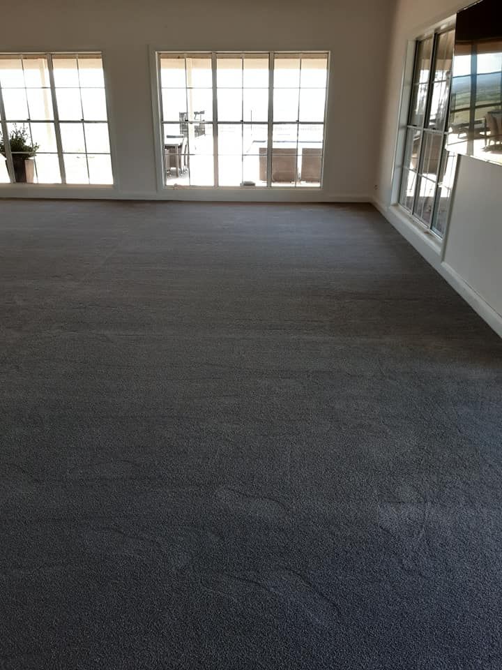 A large empty room with a gray carpet and lots of windows