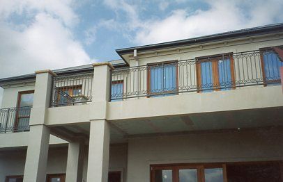 A large white house with a balcony and a blue sky in the background
