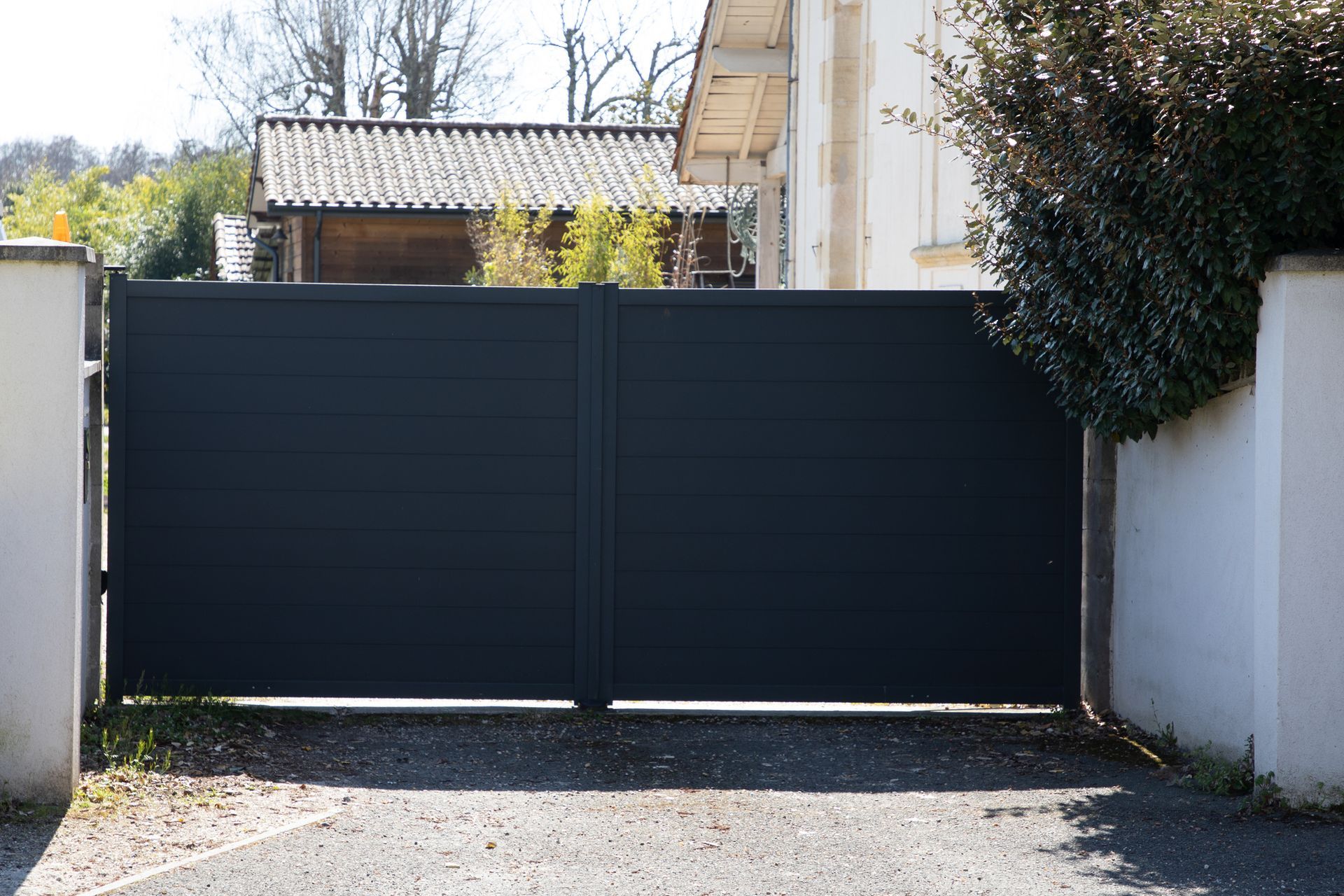 Closed black gate between white walls at a residential driveway.