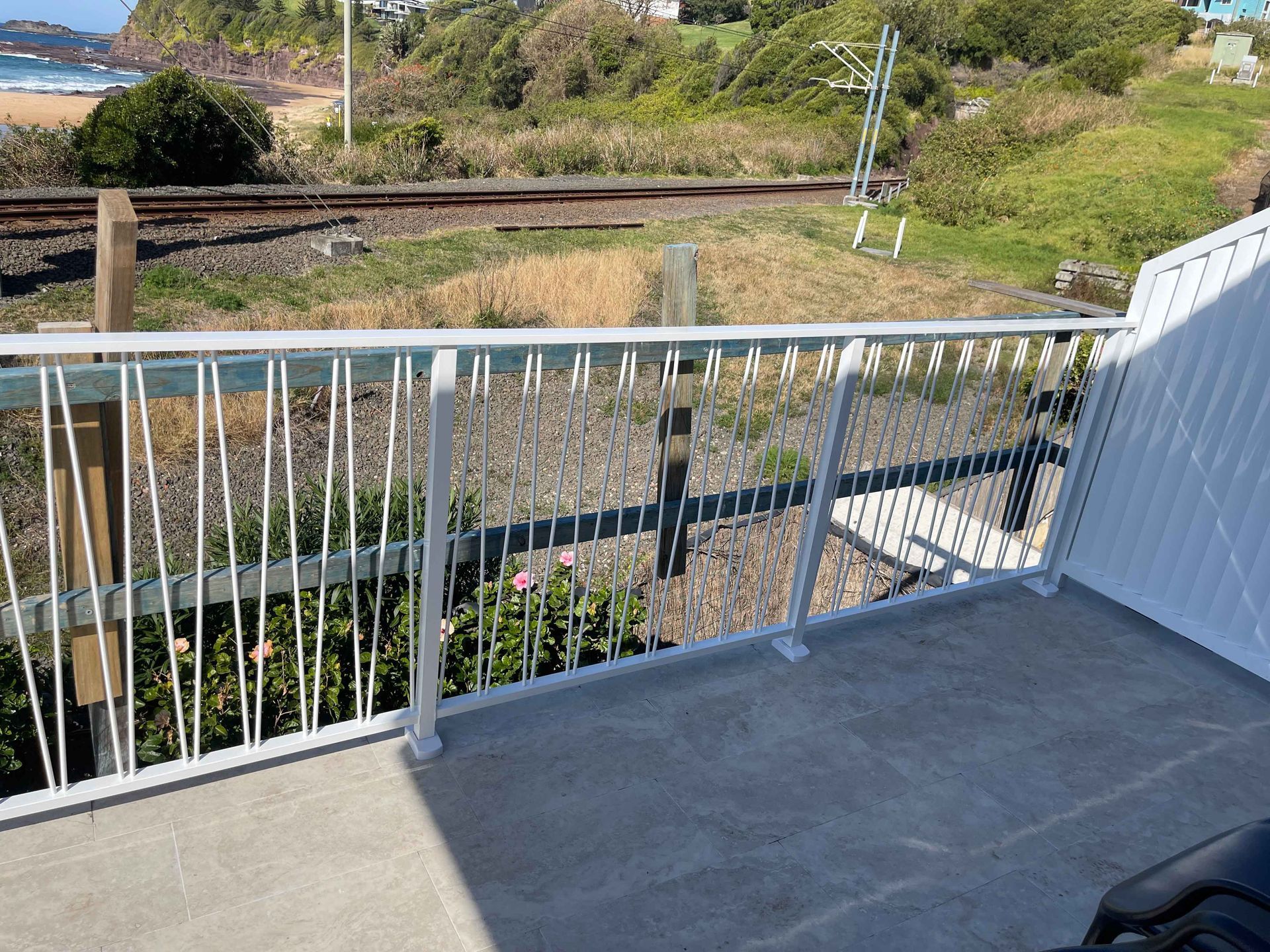 A balcony with a railing overlooking a train track and a beach.