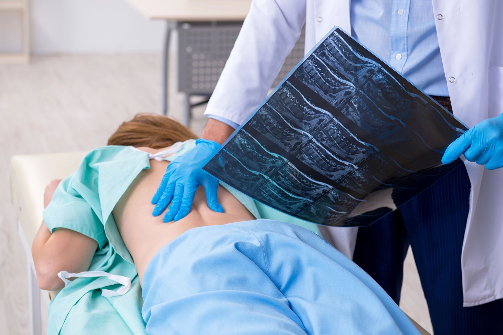 Un operatore sanitario in camice bianco e guanti blu esamina la schiena di un paziente mentre tiene in mano una radiografia.