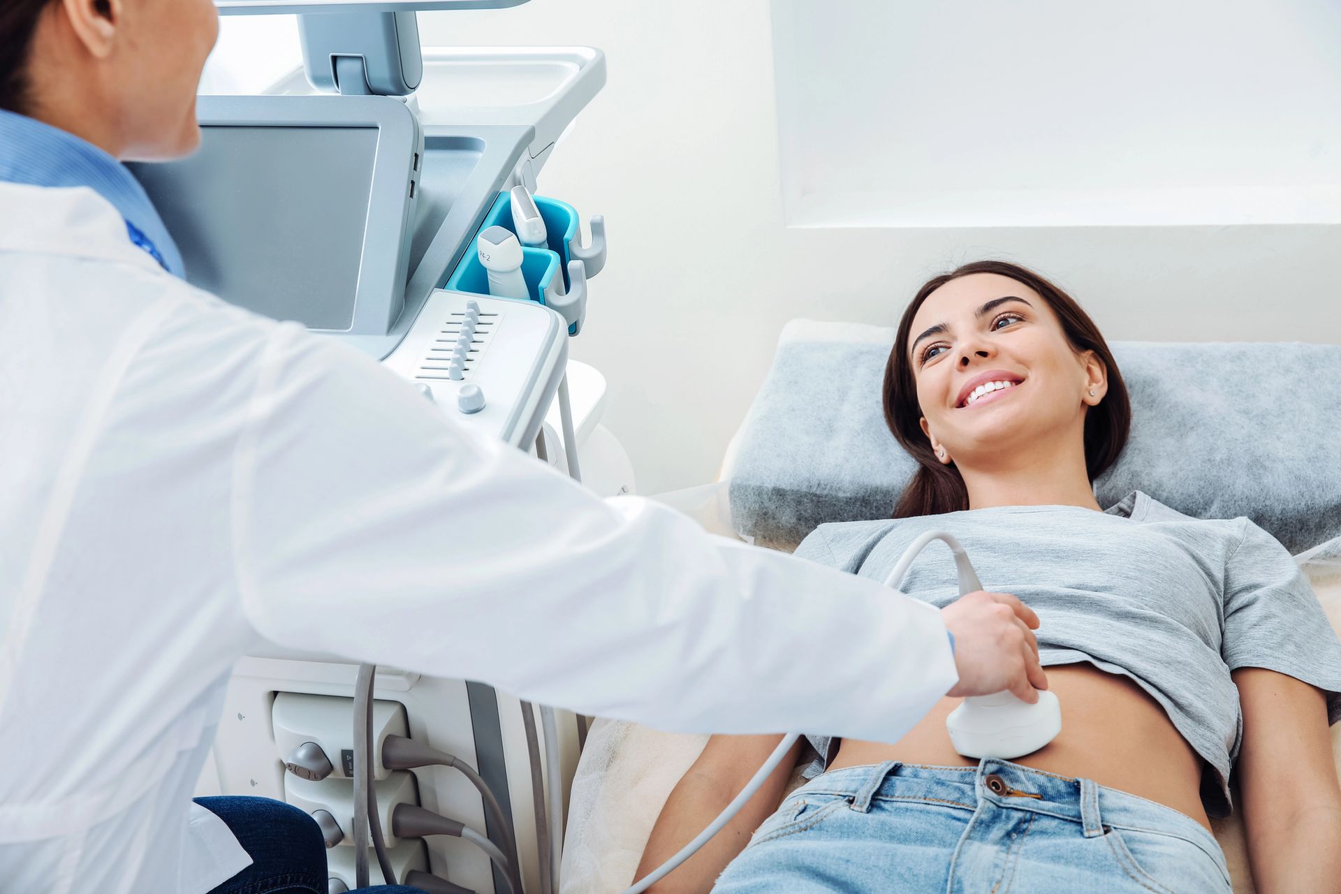 Un operatore sanitario esegue un'ecografia addominale su una paziente sorridente sdraiata su un lettino da visita in un ambulatorio.