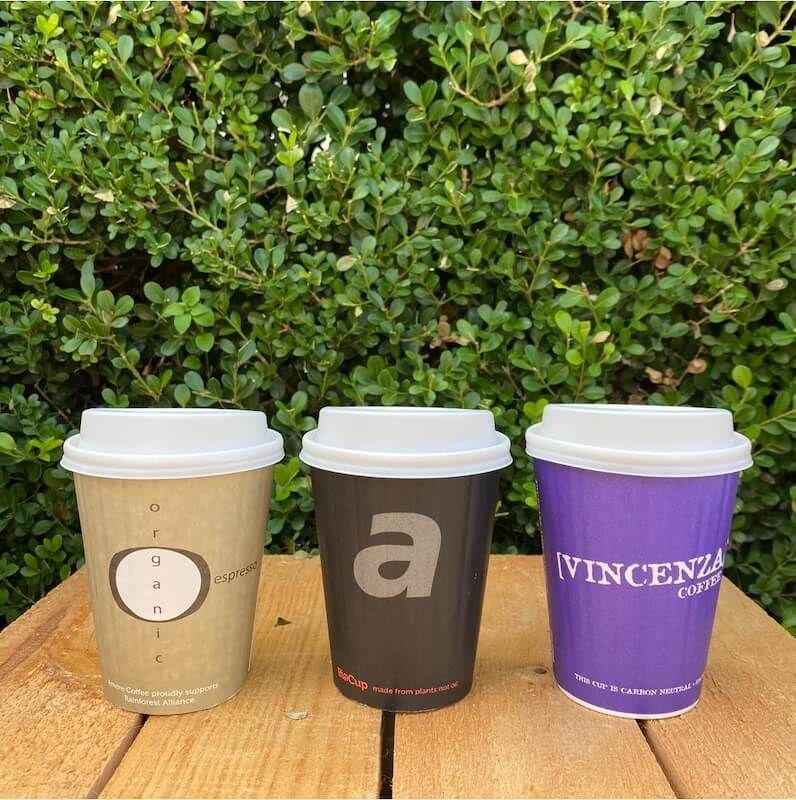 Three coffee cups are sitting on a wooden table in front of a bush — Labroco Gourmet Coffee Supplier In Forster, NSW