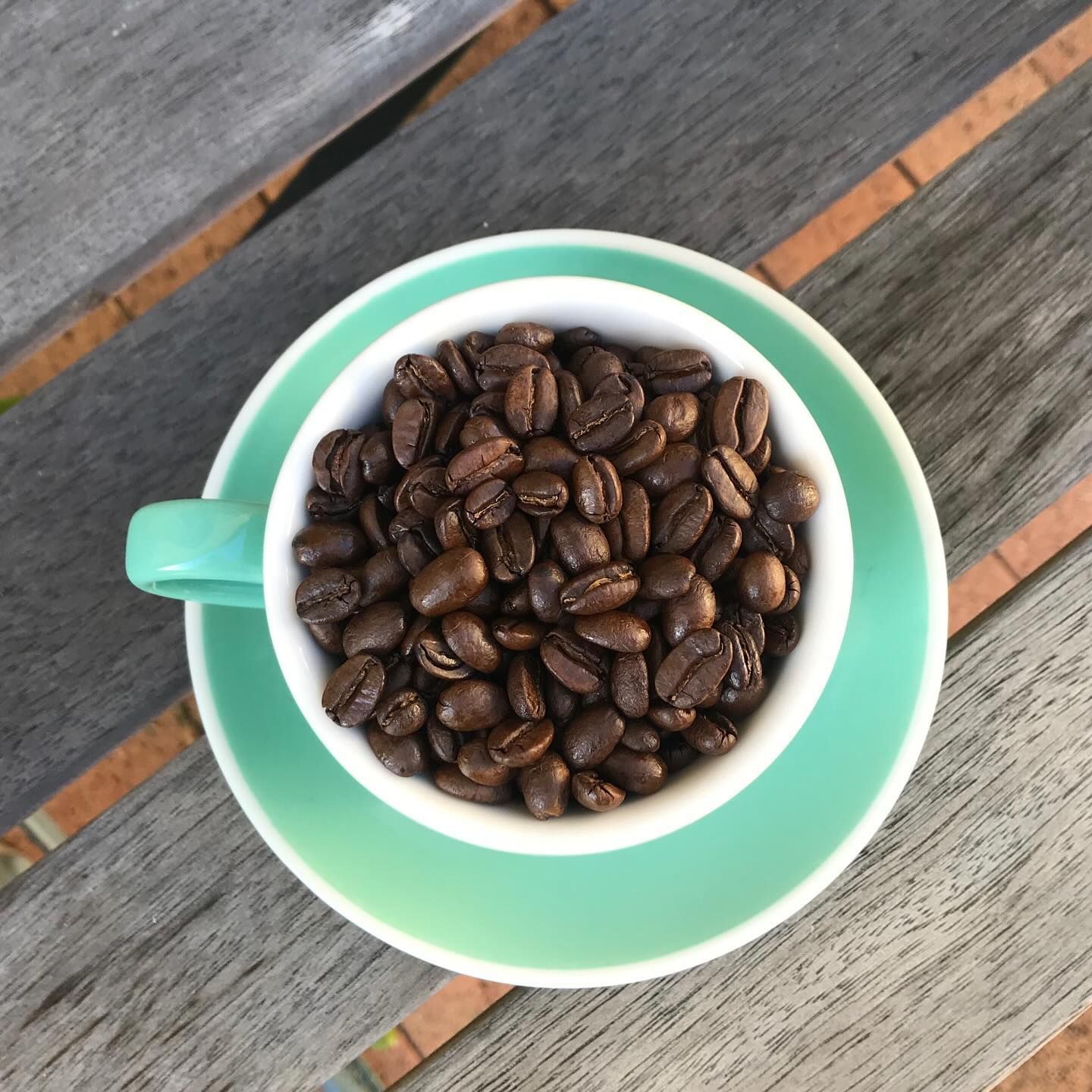A Cup and Saucer Filled With Coffee Beans on a Wooden Table — Labroco Gourmet Coffee Supplier In Forster, NSW