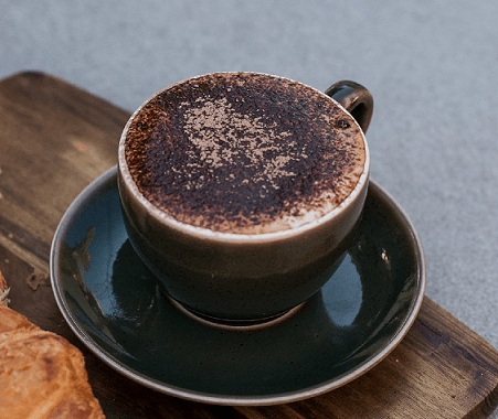 A cappuccino in a coffee cup placed on a wooden table — Labroco Gourmet Coffee Supplier In Forster, NSW