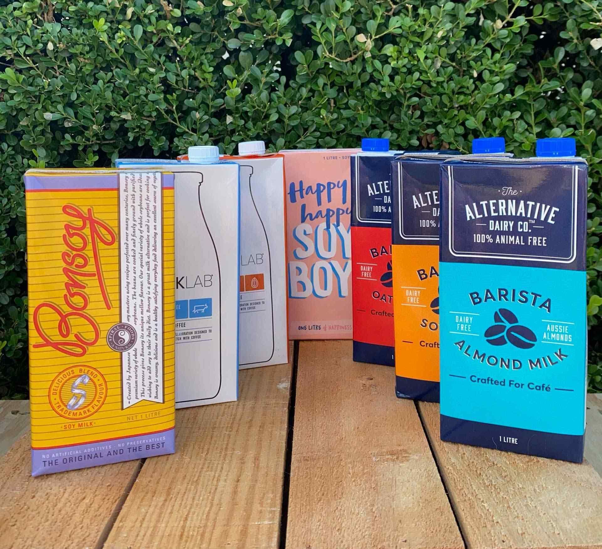 Several milk cartons in different colours, including soy, almond, and oat milk, arranged on a wooden surface — Labroco Gourmet Coffee Supplier In Forster, NSW