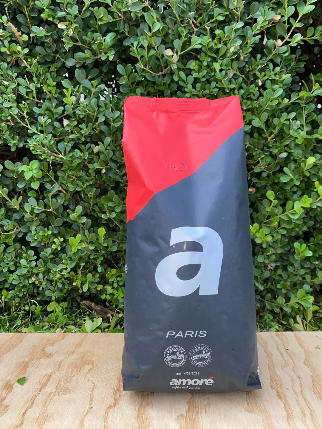 A Bag of Coffee is Sitting on a Wooden Table in Front of a Bush — Labroco Gourmet Coffee Supplier In Forster, NSW