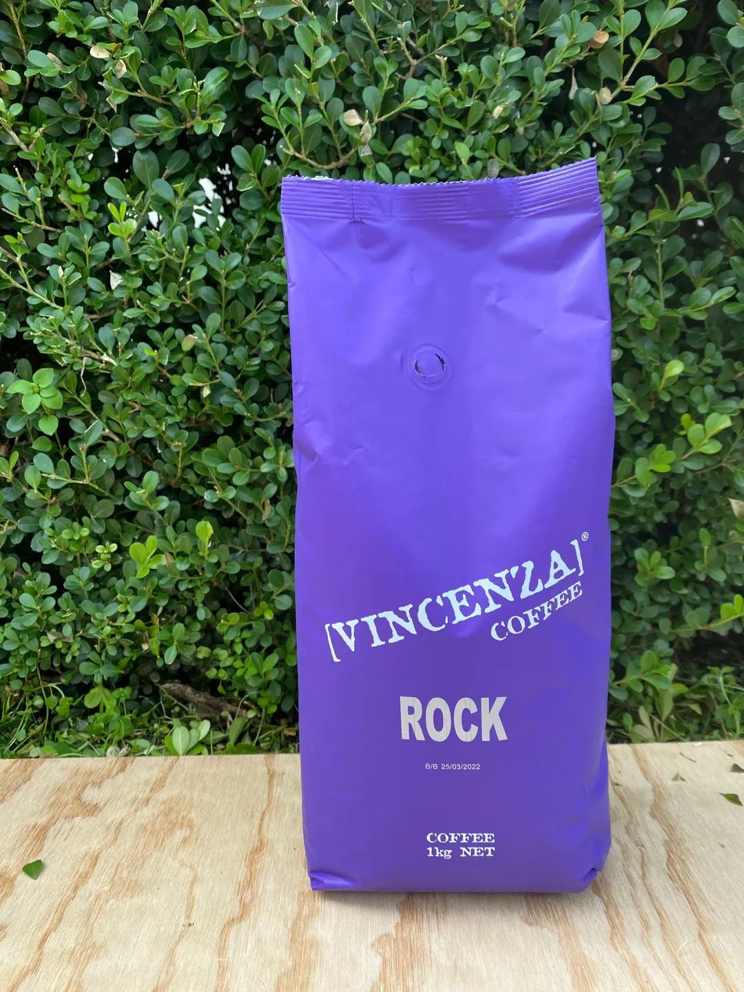 A Purple Bag of Coffee Beans is Sitting on a Wooden Table — Labroco Gourmet Coffee Supplier In Forster, NSW