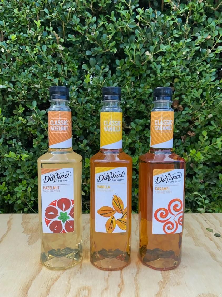 Three Da Vinci syrup bottles, flavours: Blood Orange, Mandarin, and Pumpkin Spice, outdoors on wood — Labroco Gourmet Coffee Supplier In Forster, NSW