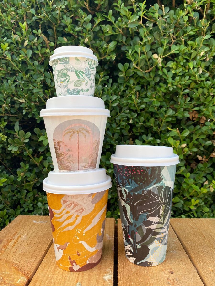 Three coffee cups are sitting on a wooden table in front of a bush — Labroco Gourmet Coffee Supplier In Forster, NSW