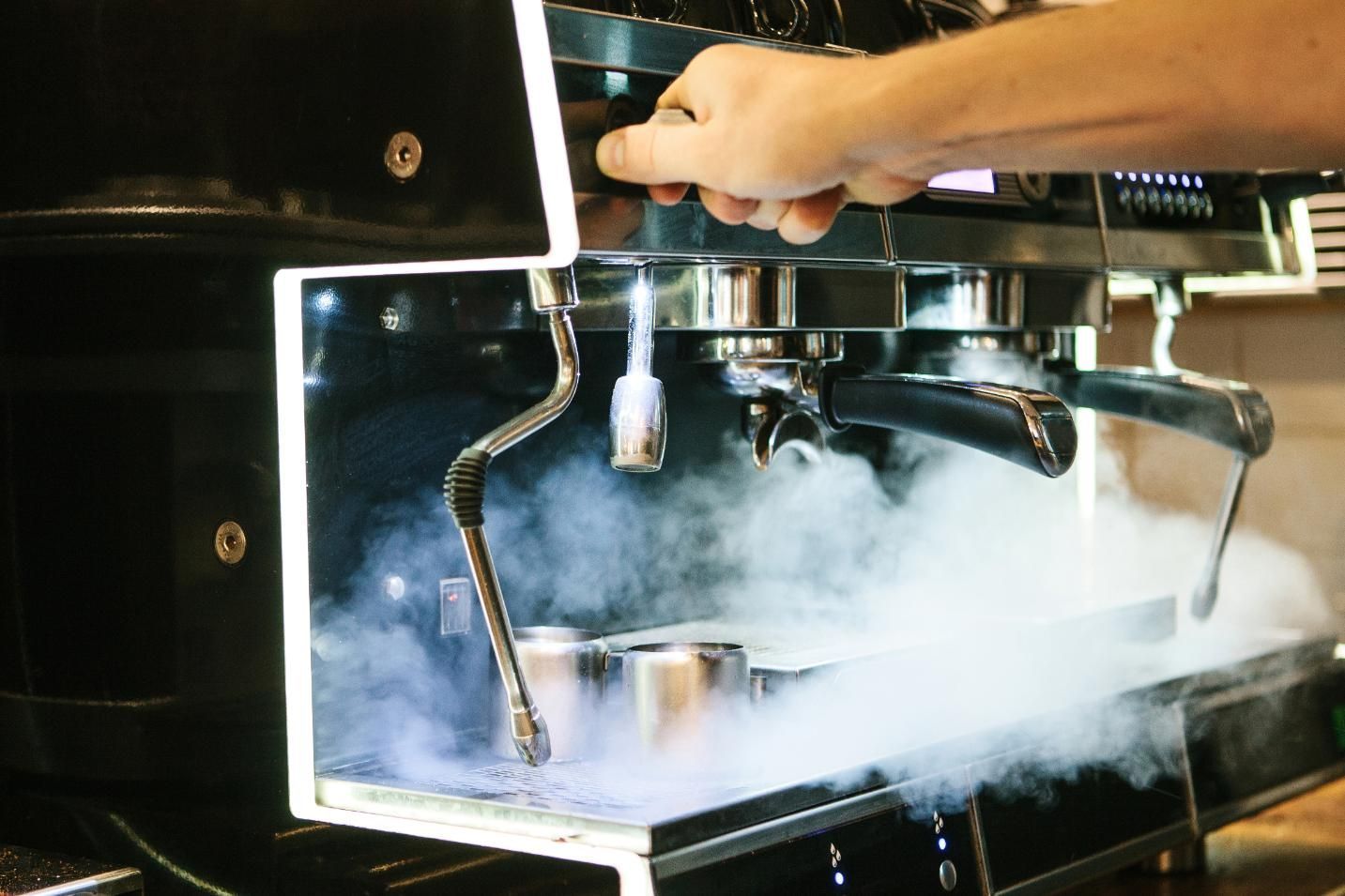 A person is using a coffee machine with steam coming out of it — Labroco Gourmet Coffee Supplier In Forster, NSW