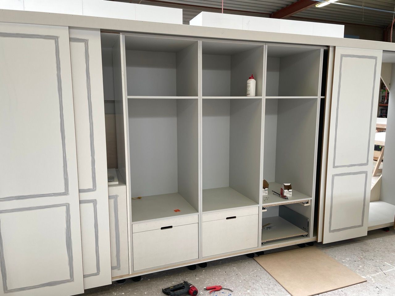 In een pakhuis wordt een grote witte kast met schuifdeuren gebouwd.