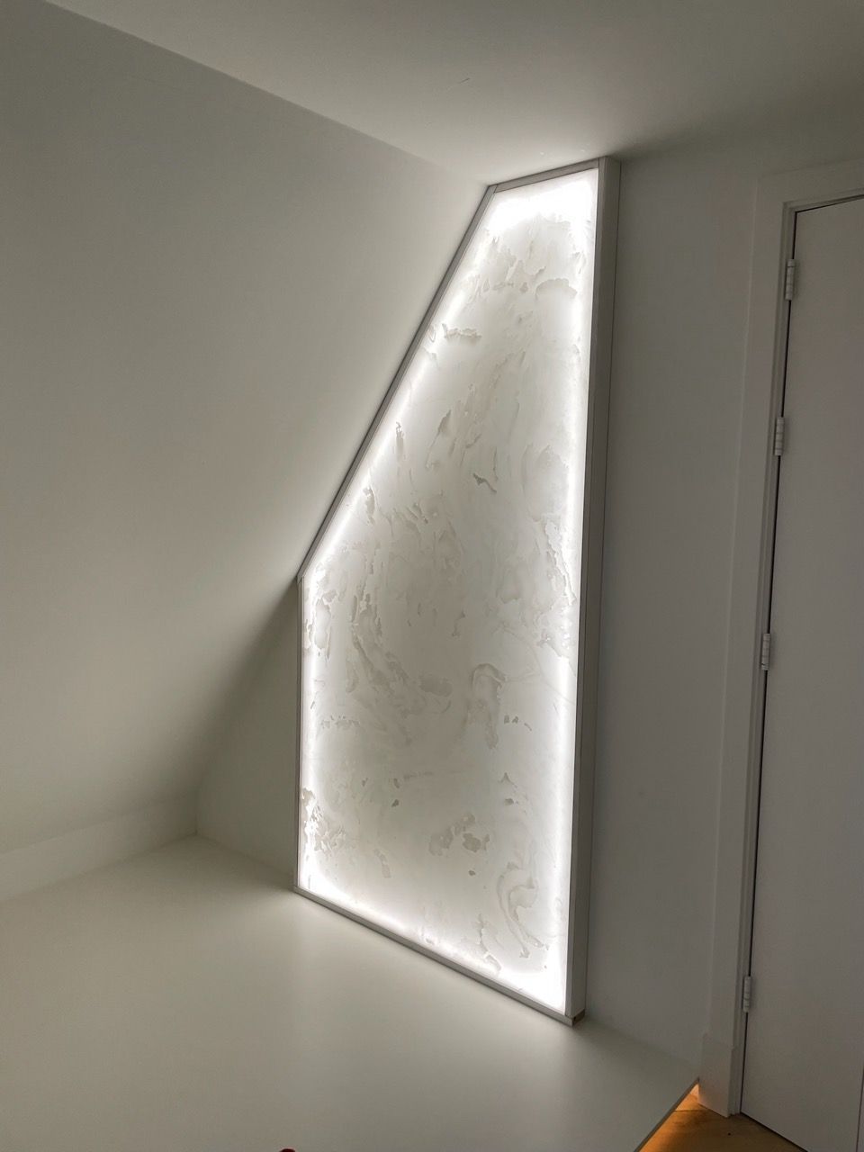 Een op maat gemaakte kast met een unieke schuine vormgeving, zorgvuldig ontworpen door Vuijst & Vuijst, verrijkt met sfeervolle, geïntegreerde verlichting. Deze kast is niet alleen een opslagwonder, maar dient ook als een opvallend designelement dat de ruimte op een bijzondere manier accentueert en verlicht, perfect afgestemd op de specifieke contouren en stijl van de kamer