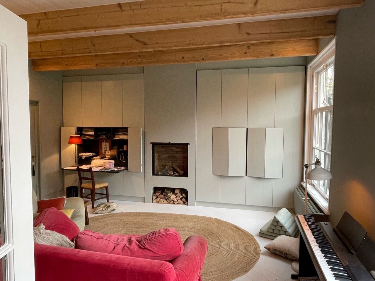 Een unieke, op maat gemaakte kast door Vuijst & Vuijst, ontworpen om naadloos op te gaan in de muur van de woonkamer, dankzij het ontbreken van handgrepen en een perfecte afstemming op de kleur van de ruimte, waardoor het lijkt alsof je naar een deel van de muur kijkt terwijl het in werkelijkheid een functionele opbergoplossing biedt.