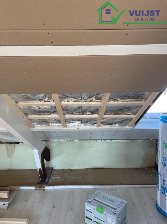 Interieurbeeld van de isolatie van een schuin dak, gezien van binnenuit de zolder. Het toont de tussen de dakspanten aangebrachte isolatiematerialen, klaar om de energie-efficiëntie te verhogen. De structuur van de houten dakspanten is duidelijk zichtbaar, met het isolatiemateriaal netjes ertussen geplaatst, wat zorgt voor een verbeterde thermische isolatie en bijdraagt aan een comfortabeler binnenklimaat.