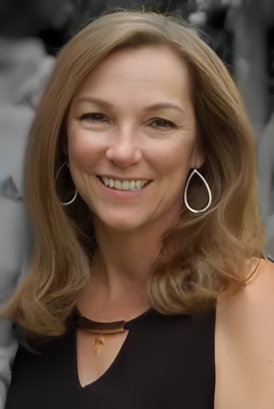 Woman with wavy blonde hair smiles, wearing white top and pearl necklace.