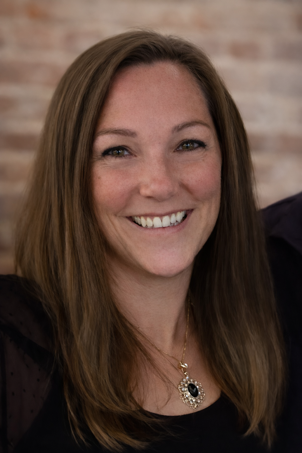 Woman with wavy blonde hair smiles, wearing white top and pearl necklace.