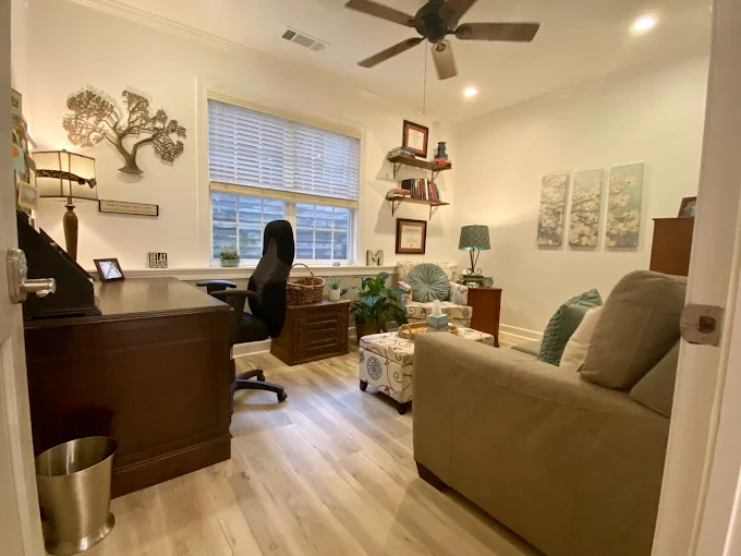 Cozy home office with a desk, chair, sofa, and window, decorated in neutral tones.