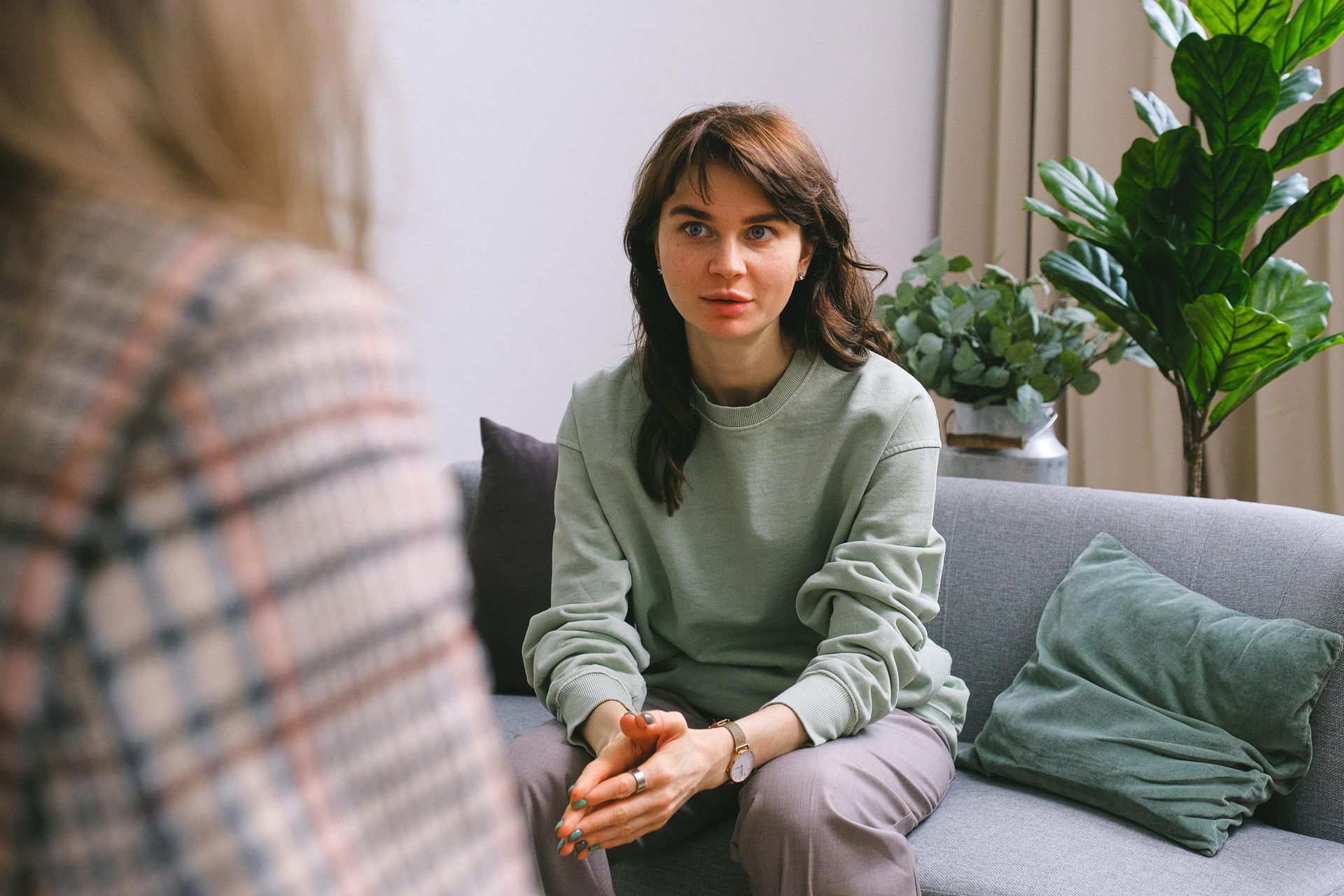 Woman in light green top talking to person out of view on couch, with plant.