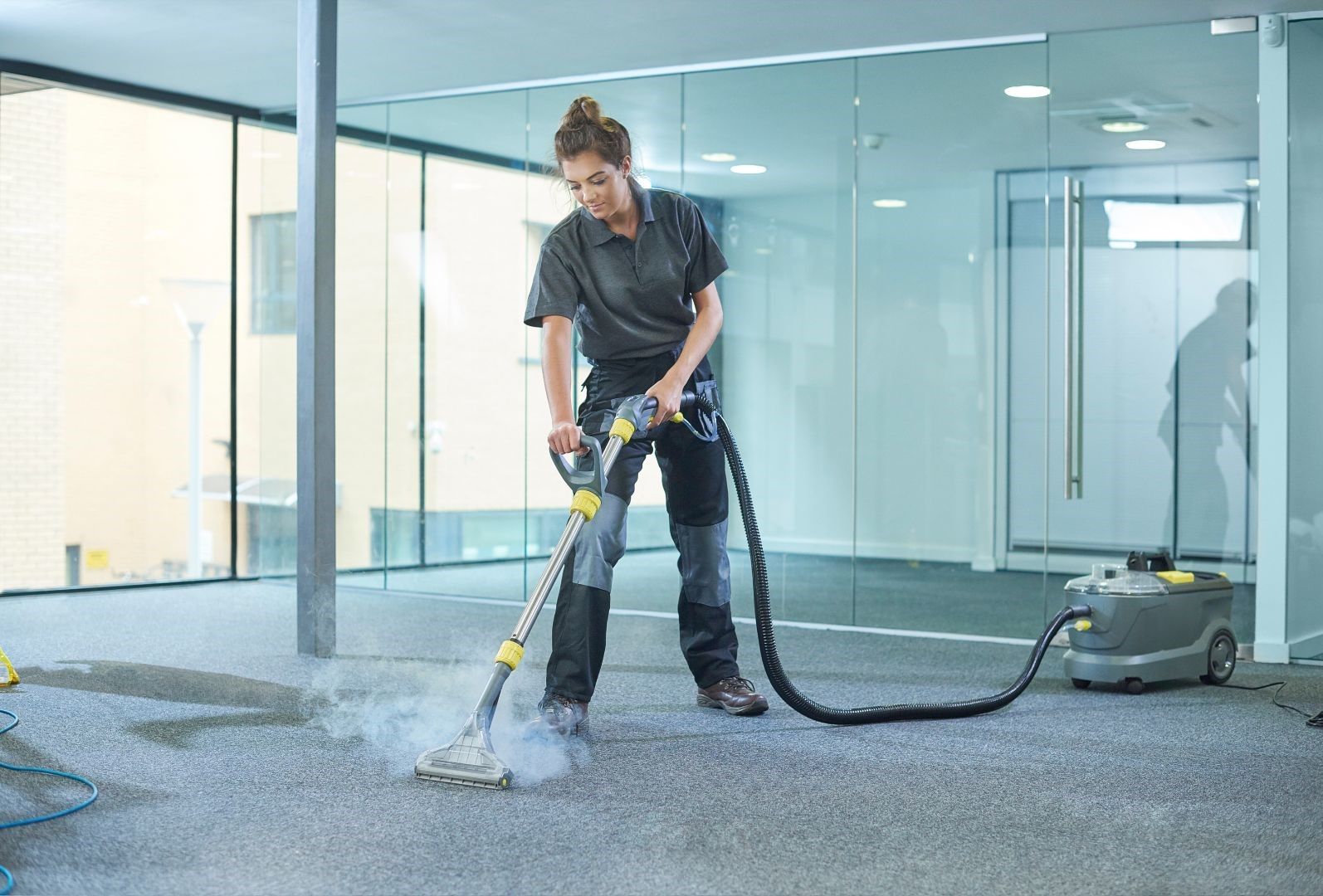 A woman is using a vacuum cleaner to clean a carpet in an office.