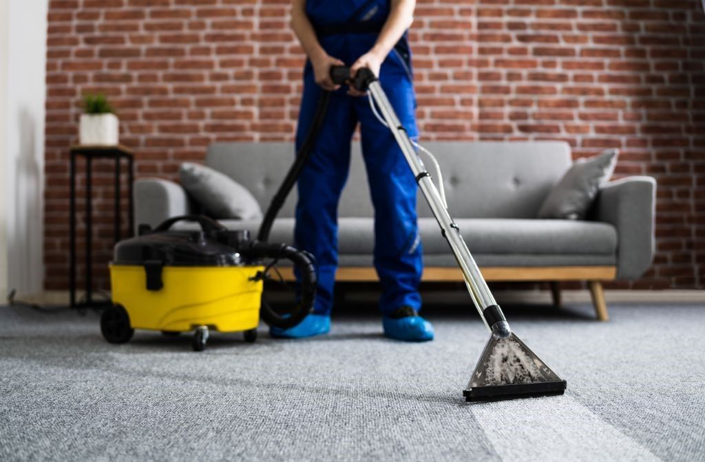 A man is cleaning a carpet with a vacuum cleaner in a living room.