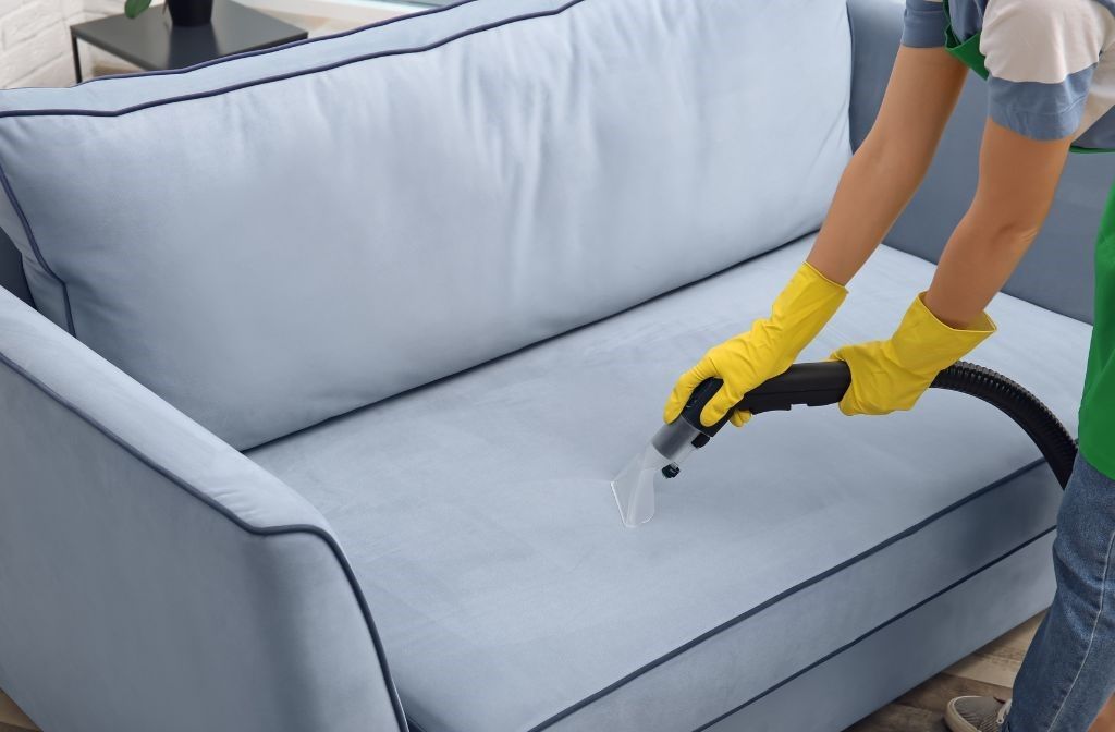 A person is cleaning a couch with a vacuum cleaner.