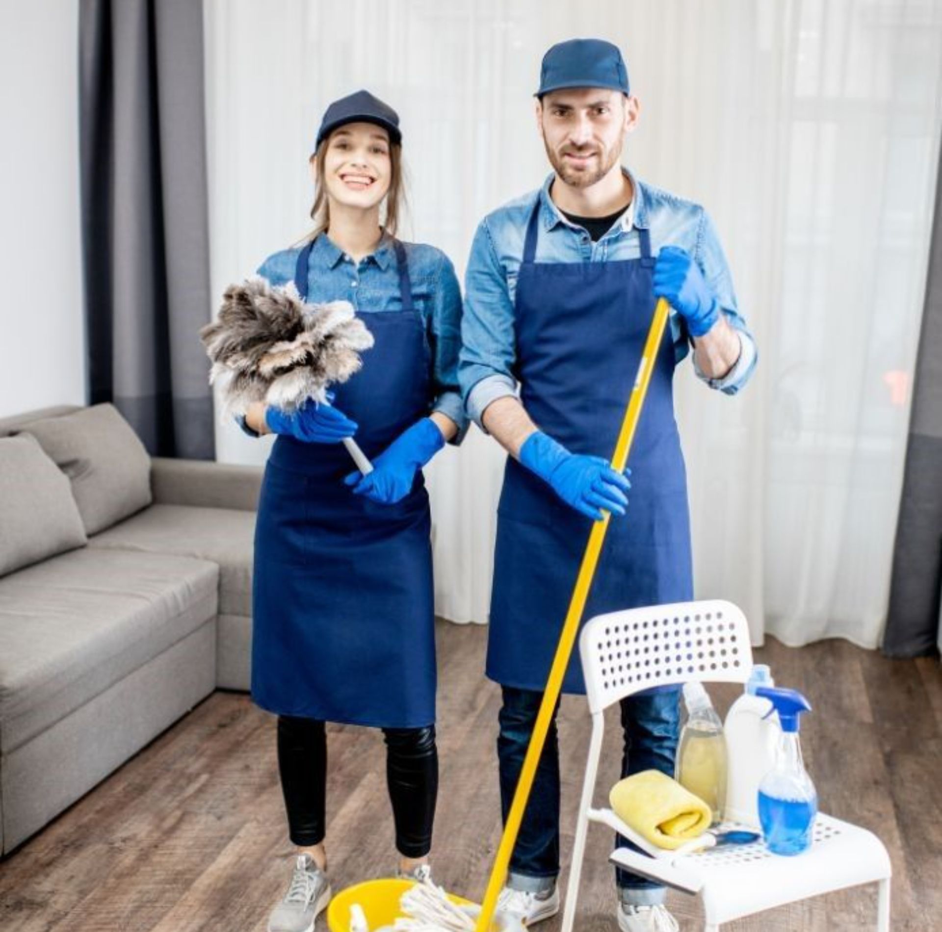 A man and a woman are standing next to each other holding mop and duster.