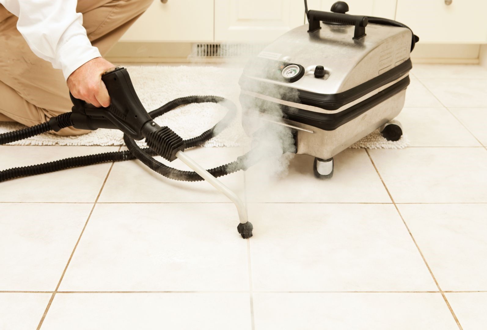 A person is using a steam cleaner to clean a tile floor.