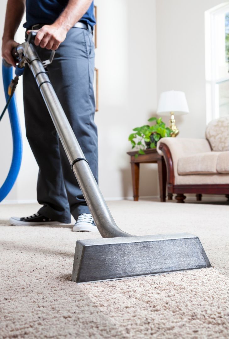 A man is using a vacuum cleaner to clean a carpet in a living room.