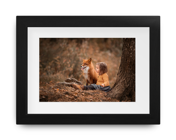 a little boy is laying under a tree with a fox .