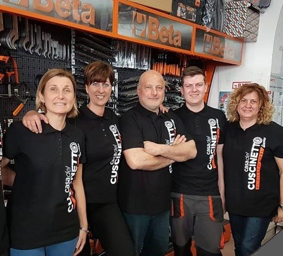 Cinque persone con camicie nere abbinate posano in un negozio di attrezzi, alcune abbracciate.