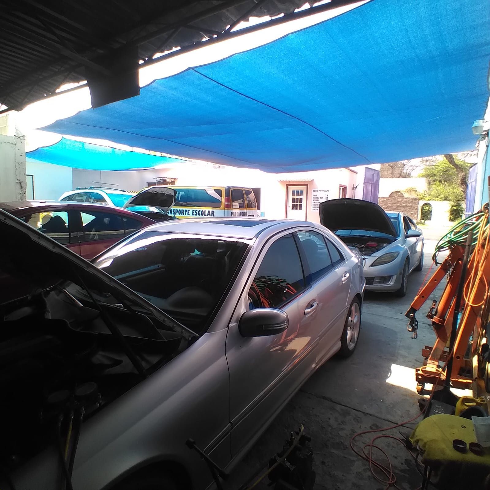 Un coche plateado con el capó levantado está aparcado bajo una lona azul.