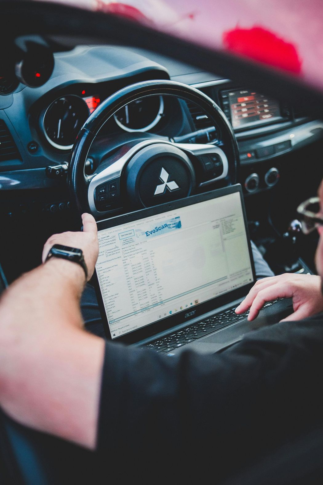 Person using a laptop inside a Mitsubishi car, likely for diagnostics or tuning. The car's interior is visible.