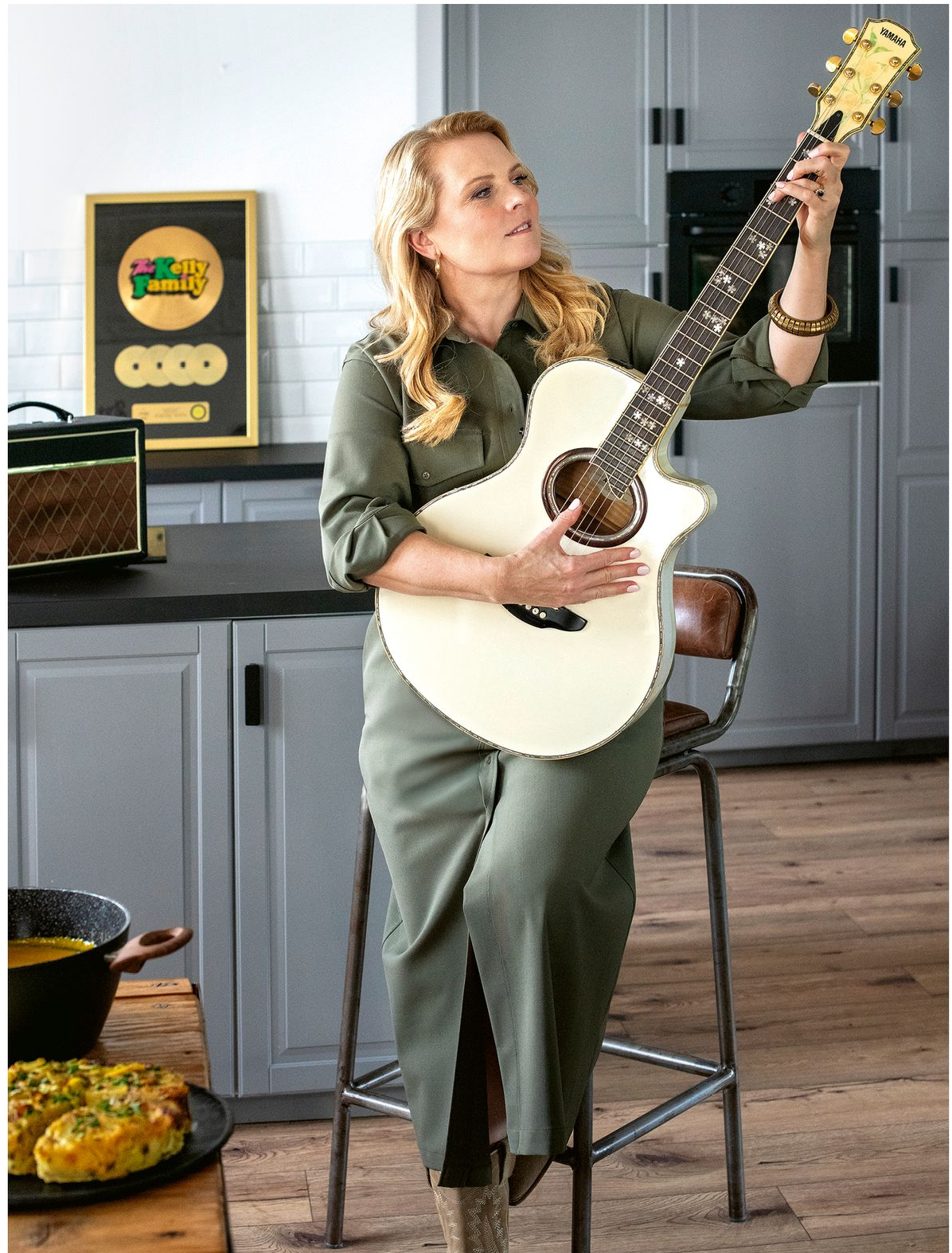 Eine Frau hält eine Gitarre vor einer Backsteinmauer