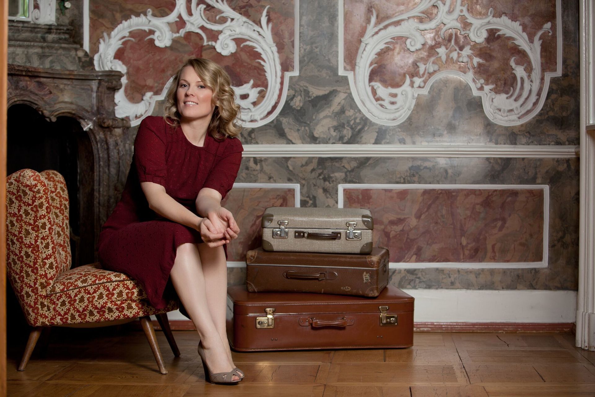 Eine Frau in einem roten Kleid sitzt auf einem Stuhl neben einem Stapel Koffer.