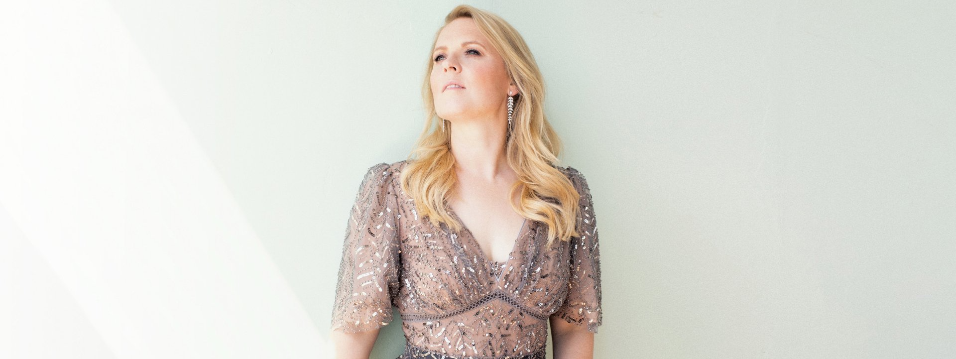 Eine Frau mit einer Blume im Haar sitzt vor einem Fenster.