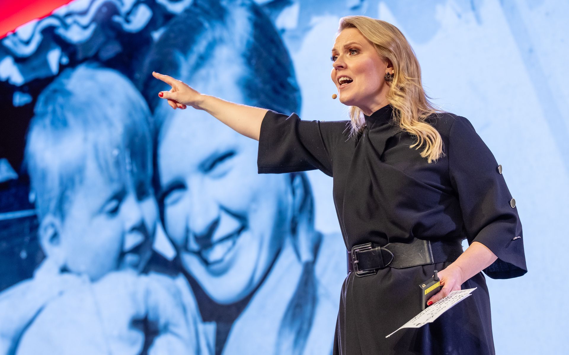 Eine Frau in einem schwarzen Kleid mit Blumen darauf steht vor einem schwarzen Hintergrund.