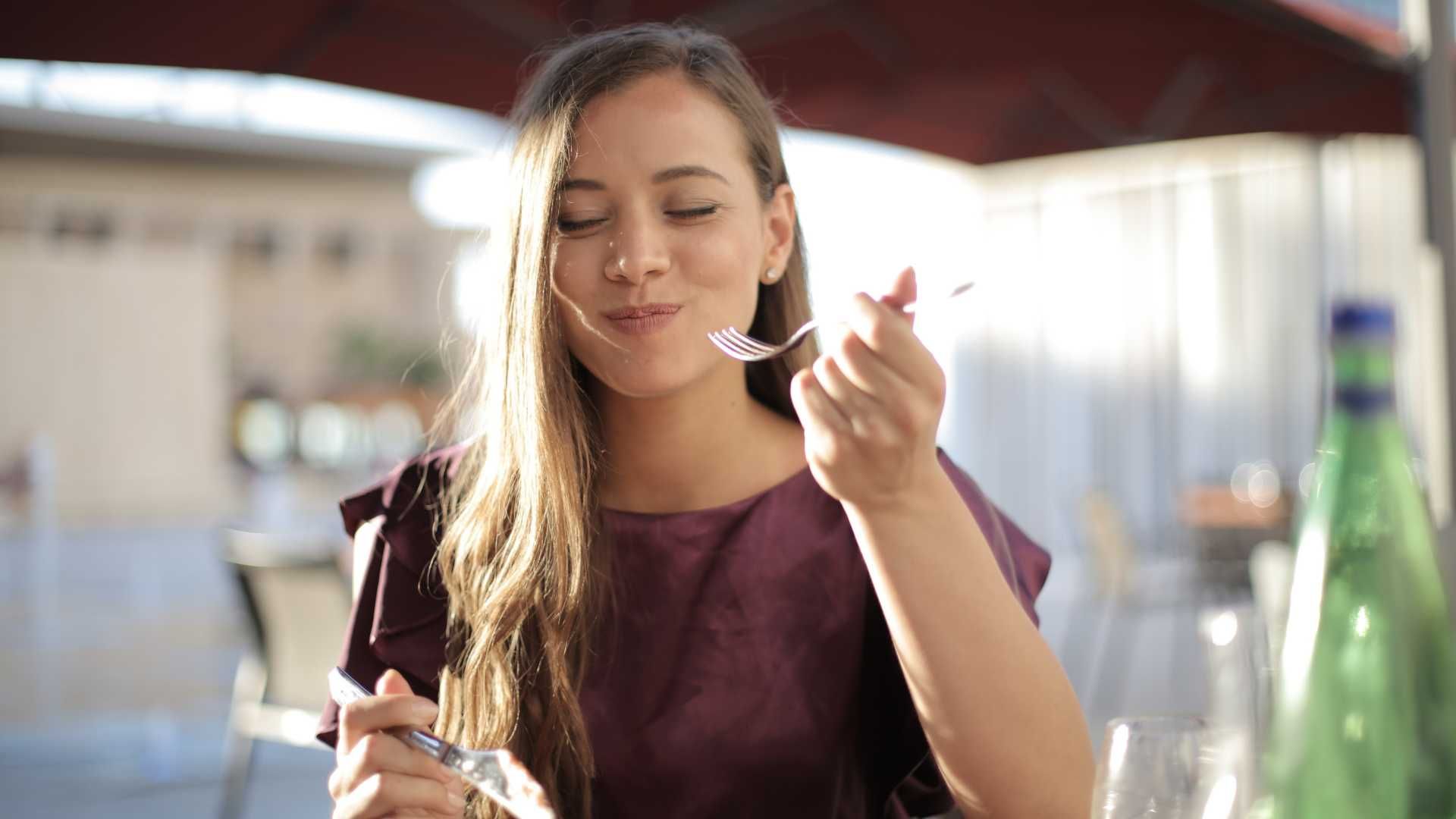 A woman is sitting at a table eating food with a fork.
